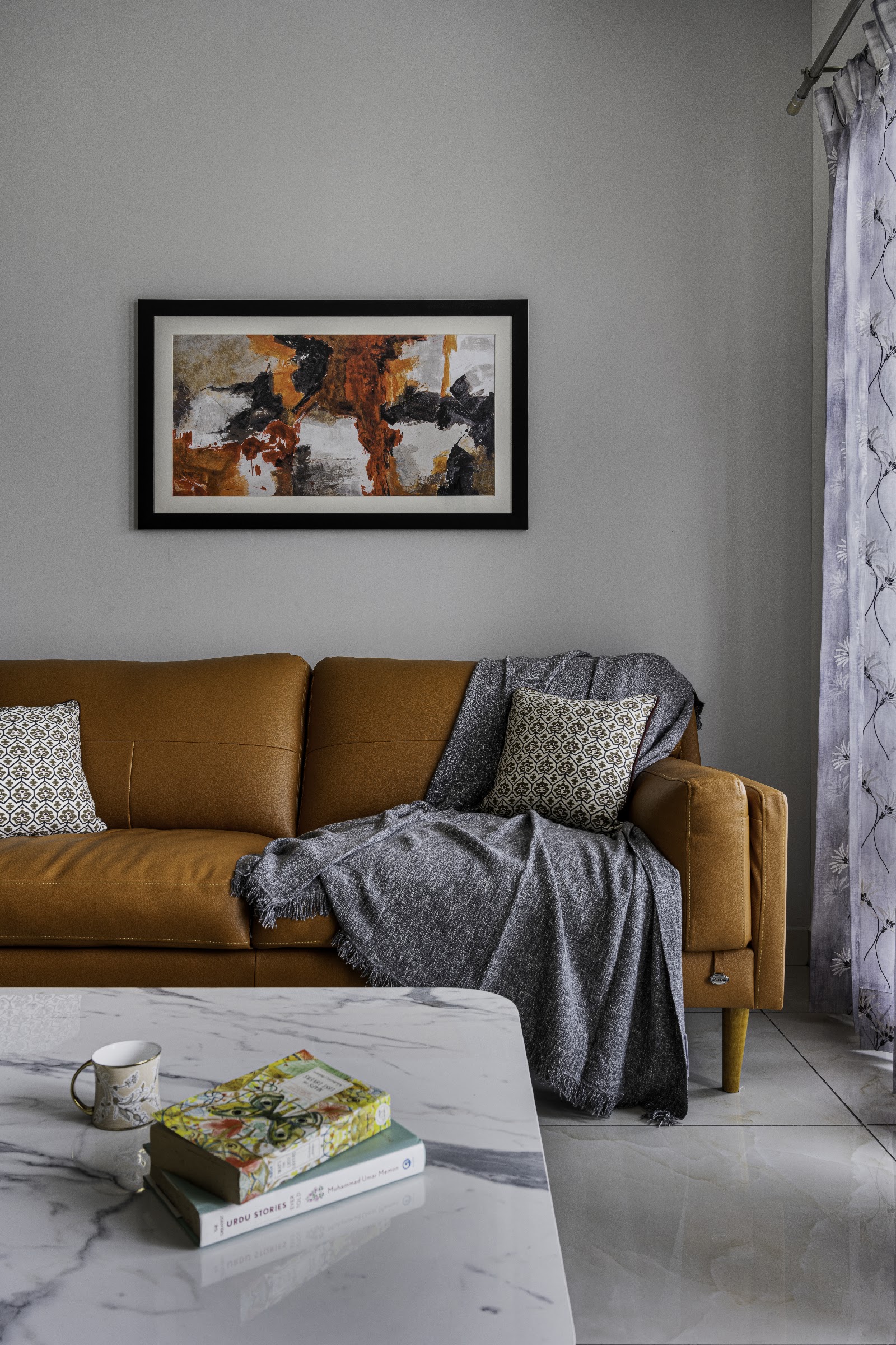 Living room vignette with a mustard leather sofa styled with a grey throw and patterned cushion beneath an abstract framed painting