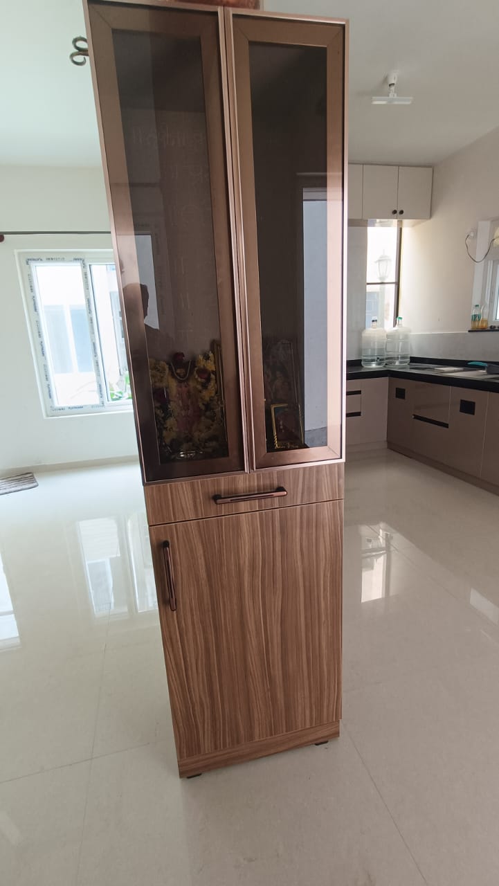 Free-standing pooja unit with tinted mirror-glass upper doors framed in rose-gold trim over a wood-grain laminate base cabinet