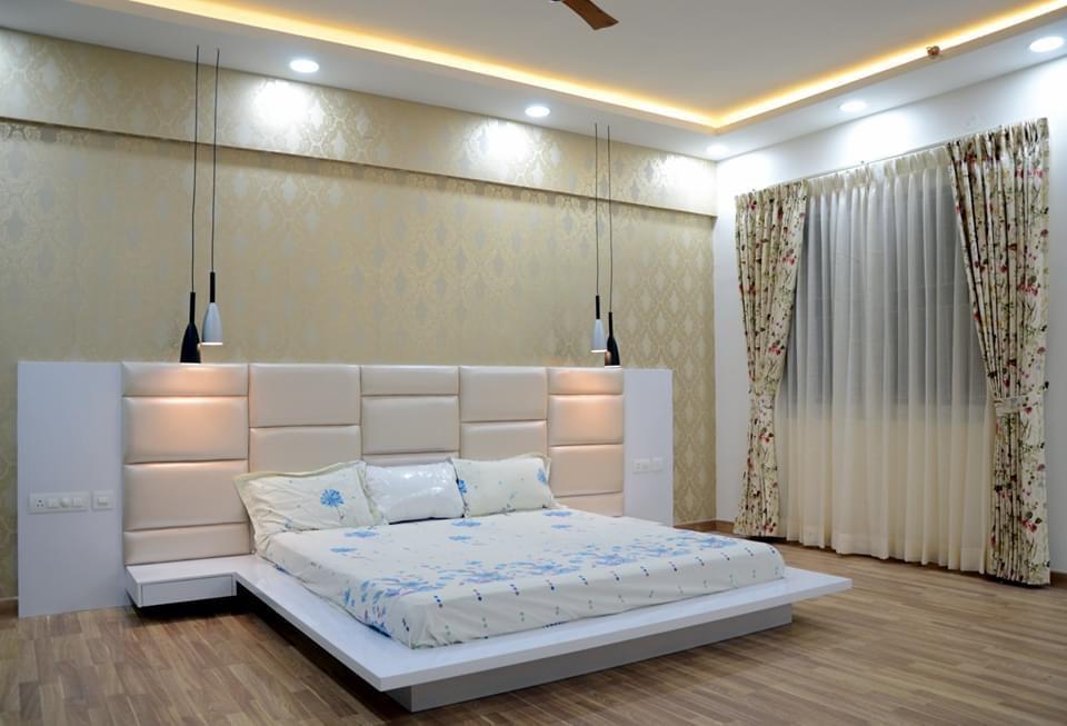 Master bedroom with a wide upholstered channel-tufted headboard wall, gold damask wallpaper, pendant lights flanking the bed