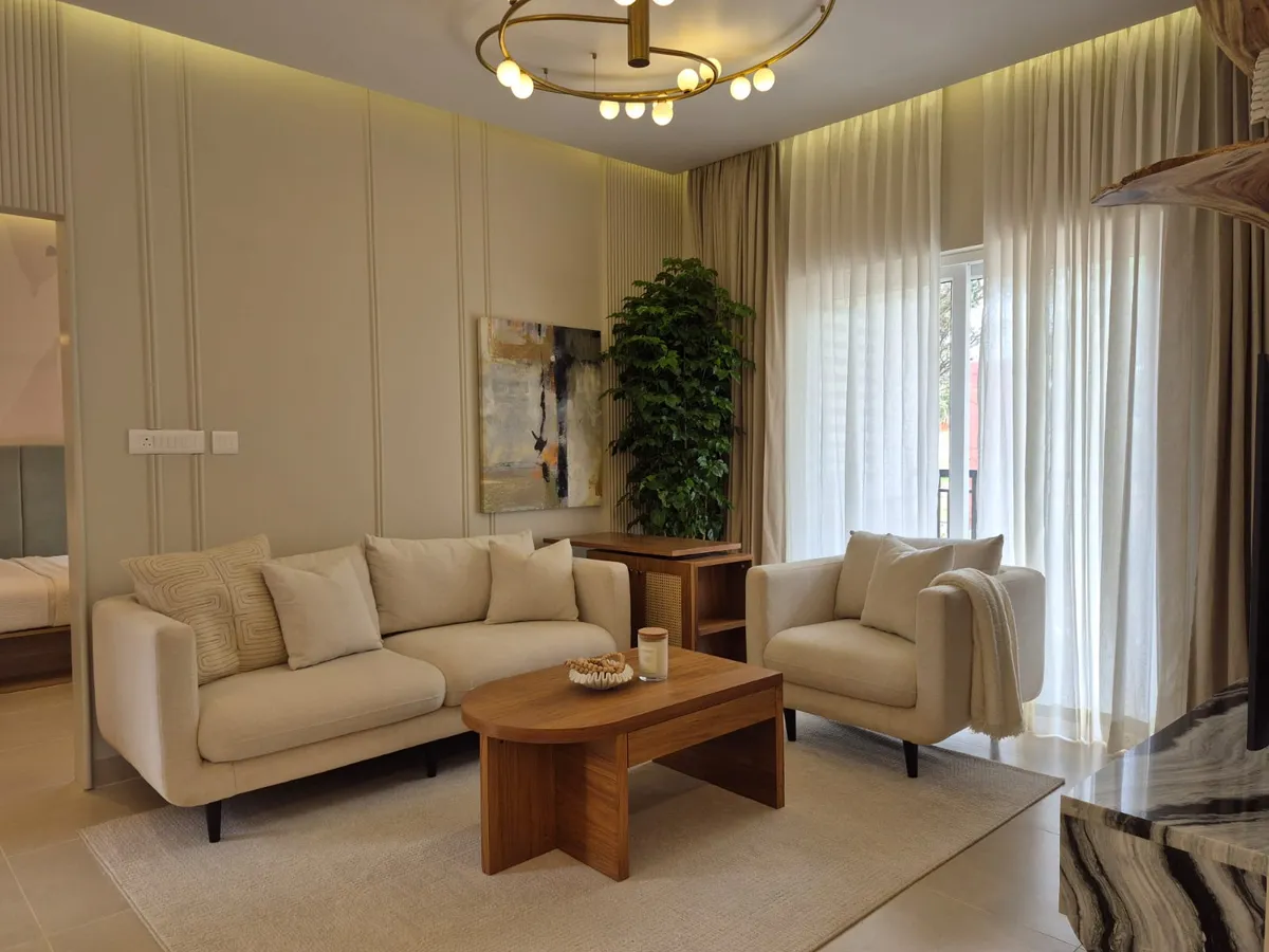 Compact living room in oatmeal fabric — three-seater and matching armchair with a throw, around a rounded teak coffee table on a jute rug