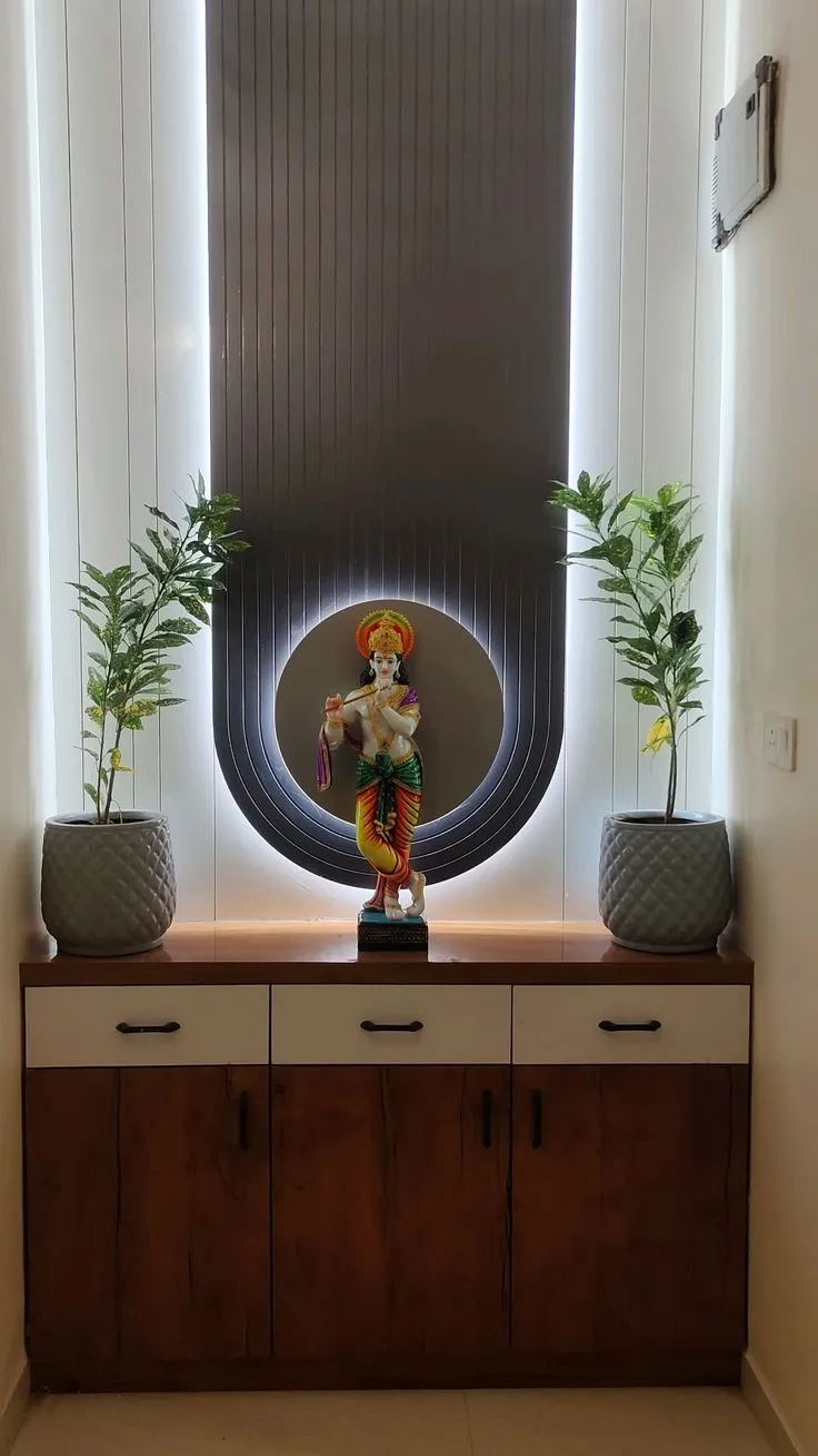 Pooja nook where a Krishna idol stands in a routed circular niche cut into a backlit dark fluted panel