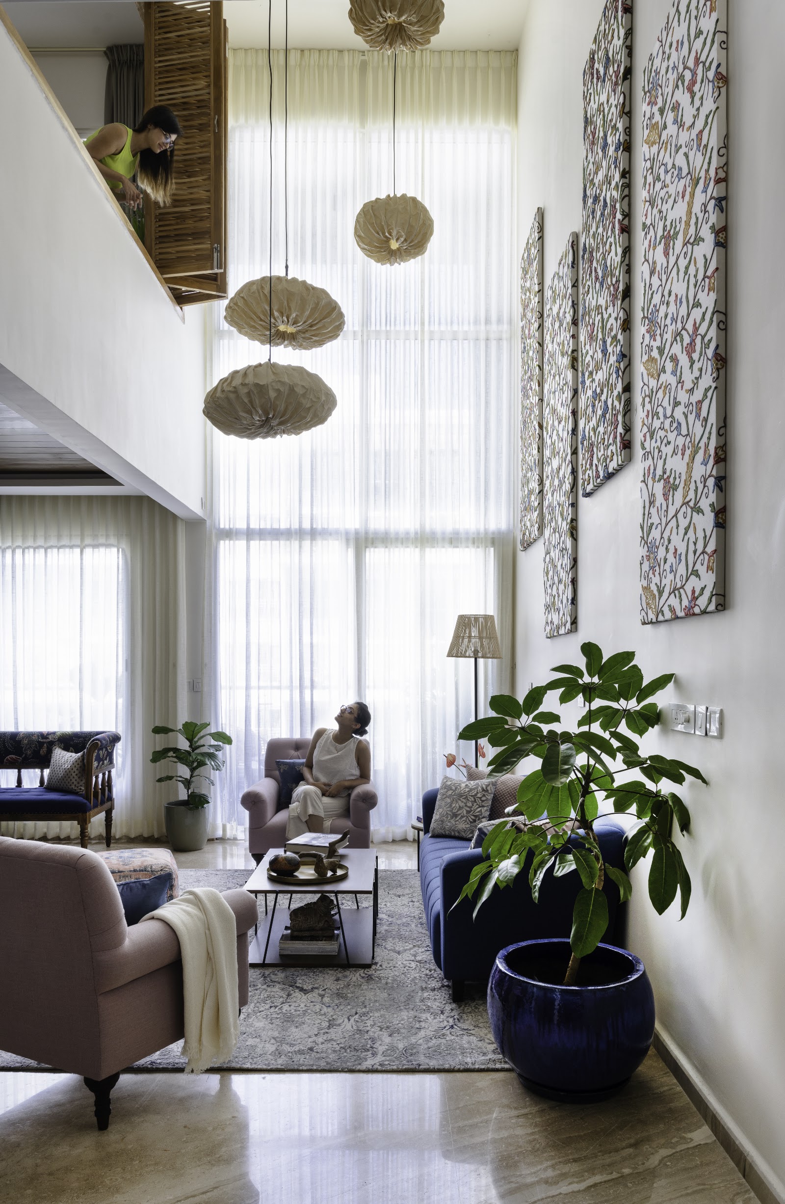 Double-height living room with sculptural paper pendant lights, embroidered floral wall panels, a navy velvet sofa