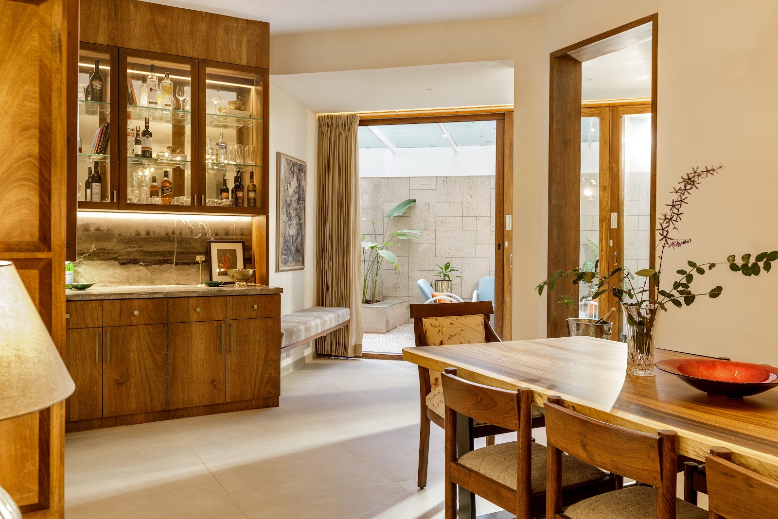 Dining room with a live-edge wood table and chairs beside a glass-front backlit bar cabinet with a marble backsplash, a full-height mirror panel