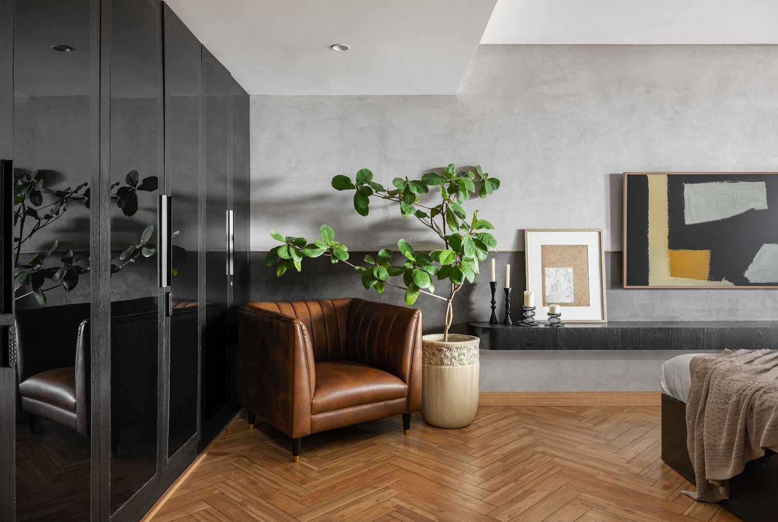 Bedroom corner with a tan leather channel-back armchair beside a large potted fig tree, a herringbone wood floor, textured concrete-look walls
