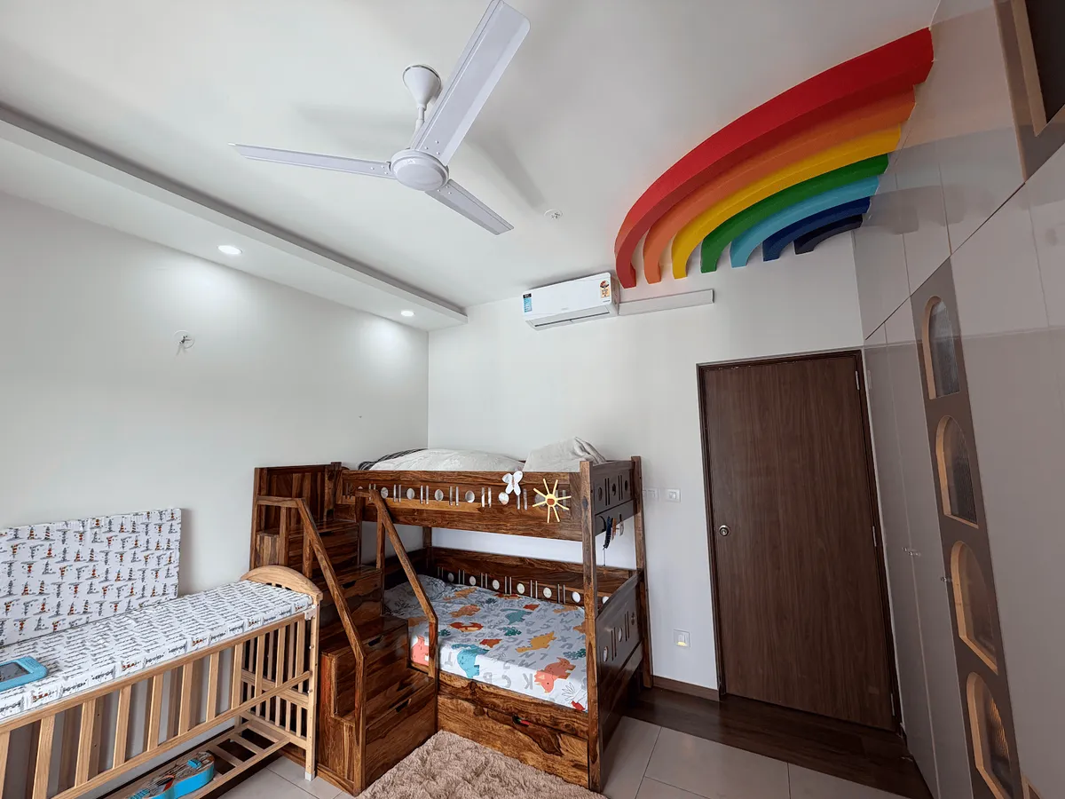 Children's room with a solid sheesham bunk bed and step-drawer staircase next to a wooden cot, under a layered rainbow sculpture mounted above the split AC