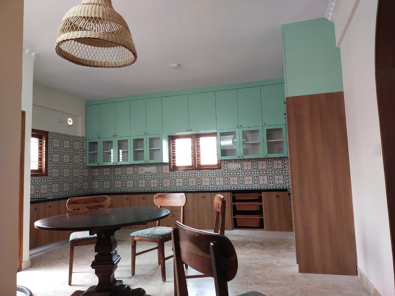 Kitchen with mint-green upper shutters, a patterned tile backsplash, and a round wood dining table with a woven rattan pendant light.