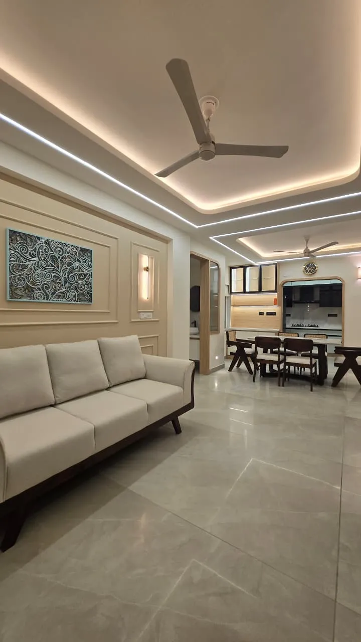 Open living room with a teak-framed cream three-seater against a wall of slim mouldings and a teal carved-motif canvas