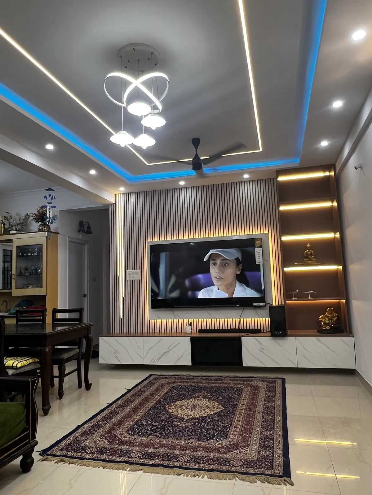 Real living room with a fluted wood TV feature wall with a backlit marble panel, a floating marble-effect TV console, lit display shelving with idols