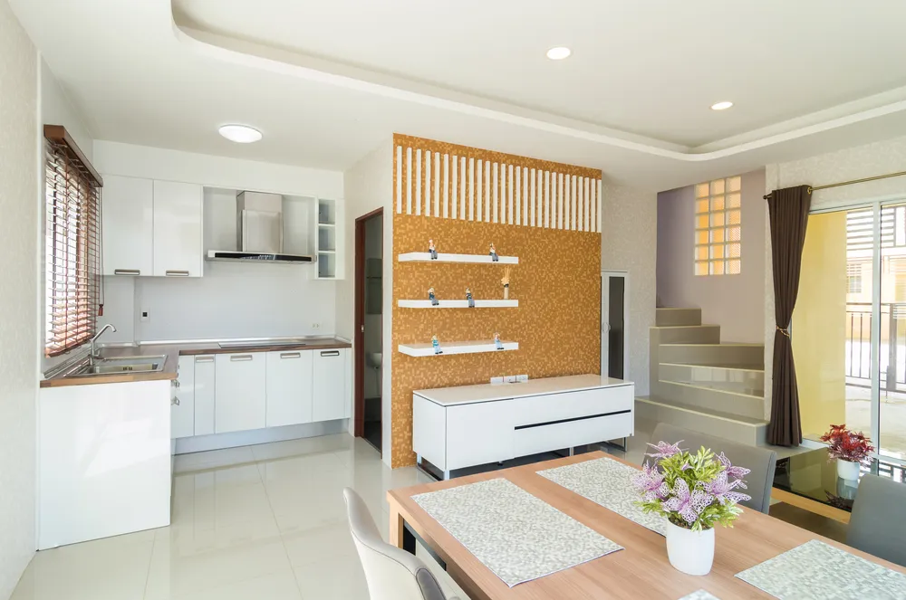 Open-plan kitchen, dining and stair landing with a mustard textured accent wall and white gloss kitchen cabinetry.