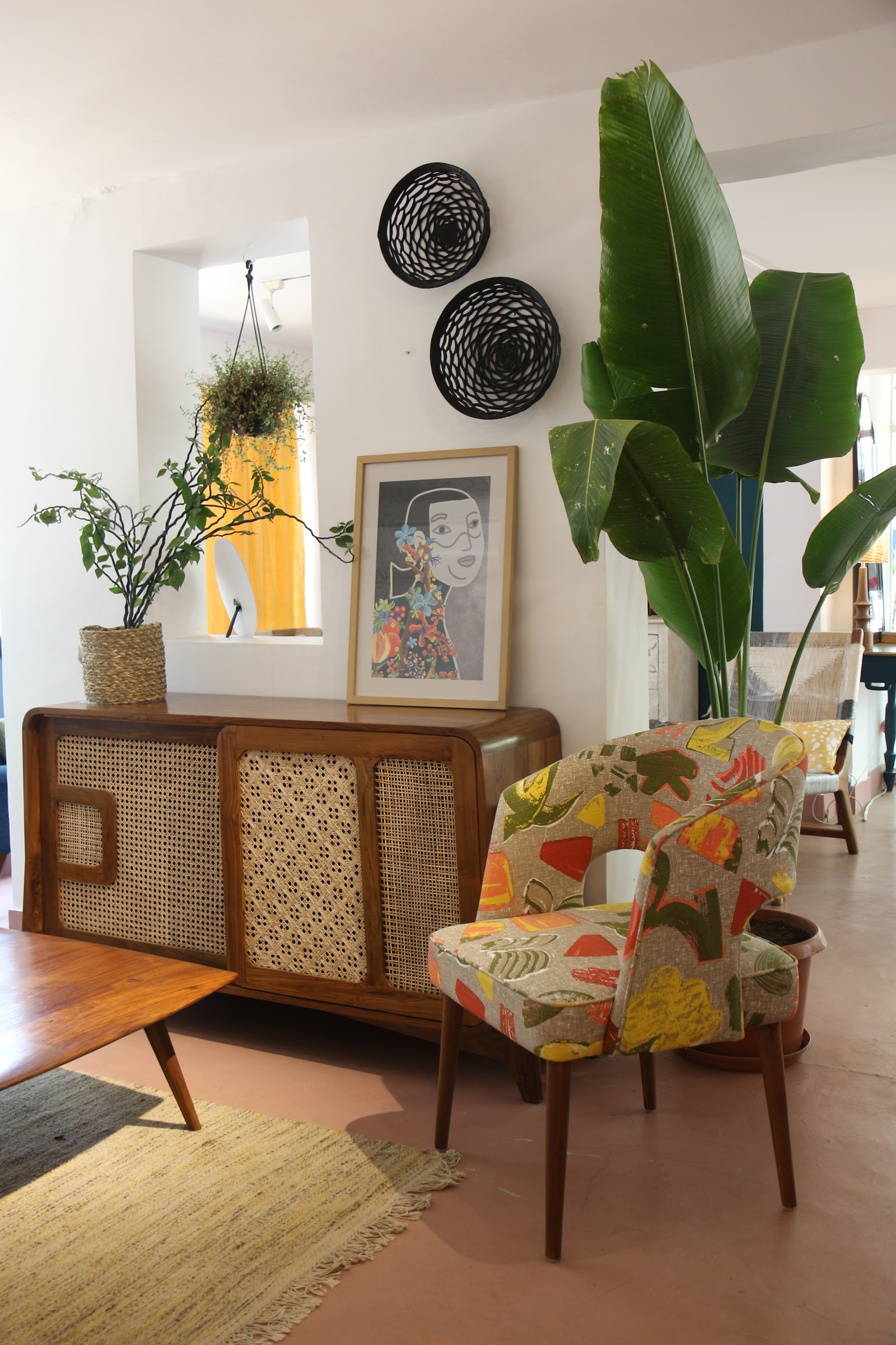 Boho-styled living room corner with a curved cane-front wood sideboard, a floral-print accent armchair, a large banana-leaf plant