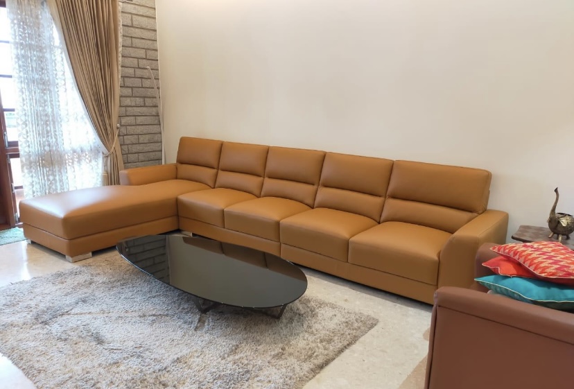 Living room with a tan leather L-shaped sofa around an oval black glass coffee table on a cream shag rug