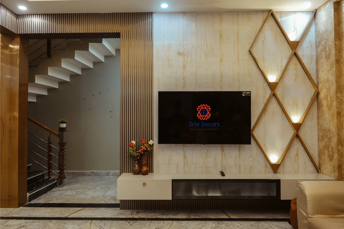 Living-room TV wall of gold-veined marble slab carrying a brass diamond lattice lit from inside its frames, flanked by full-height fluted wood panels