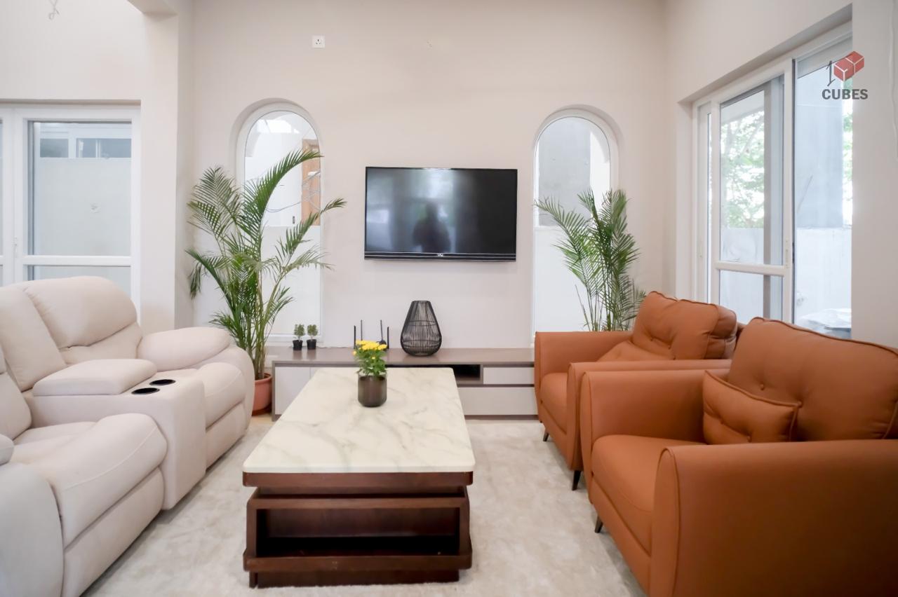 Living room with arched window surrounds, a cream reclining sofa opposite terracotta leather armchairs, and a white marble-top coffee table on a dark wood base.