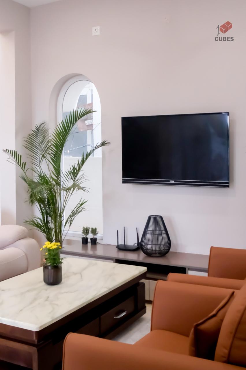 Living room with rust leather armchairs, a marble-top coffee table and a wall-mounted TV above a low console beneath an arched window