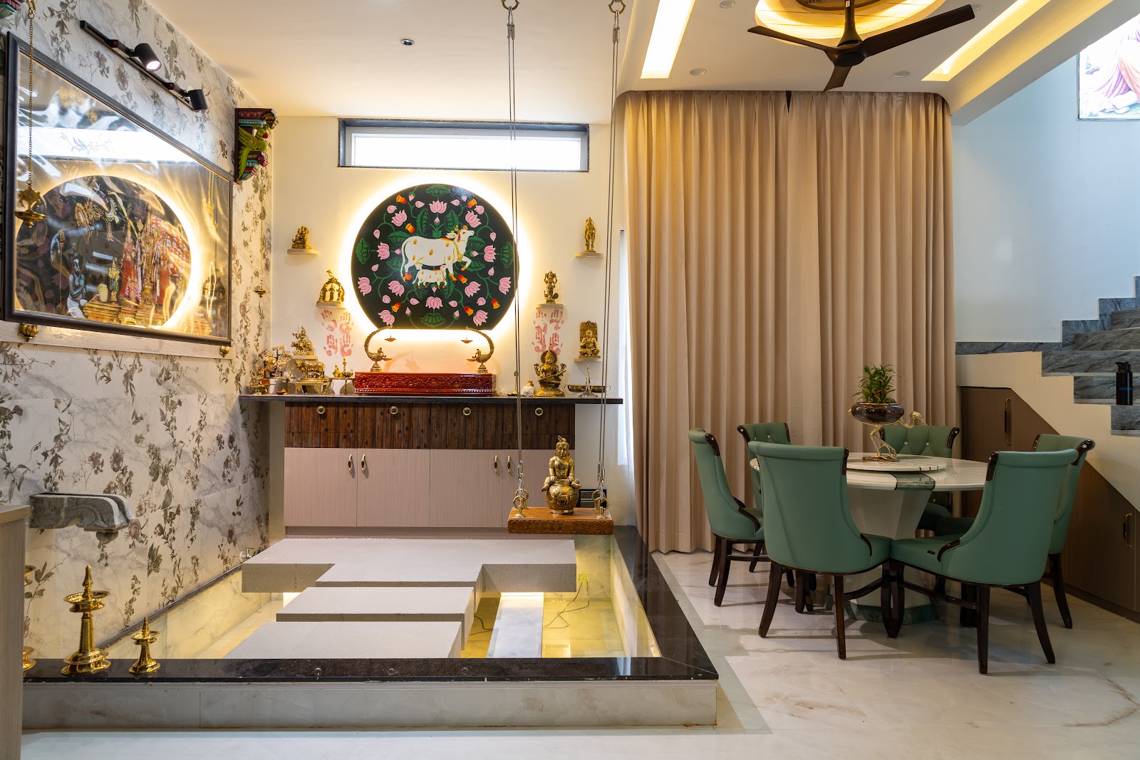 Traditional pooja room with a backlit floral shrine niche, a hanging brass oonjal swing, a wood console laid with brass ritual items