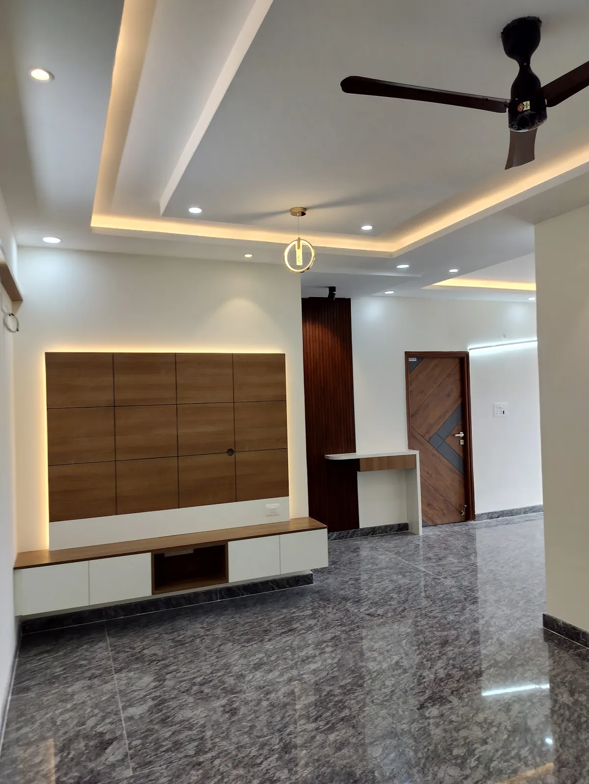Empty living room with a backlit teak panel routed into a four-by-three grid above a white-and-wood floating console, a small brass ring pendant
