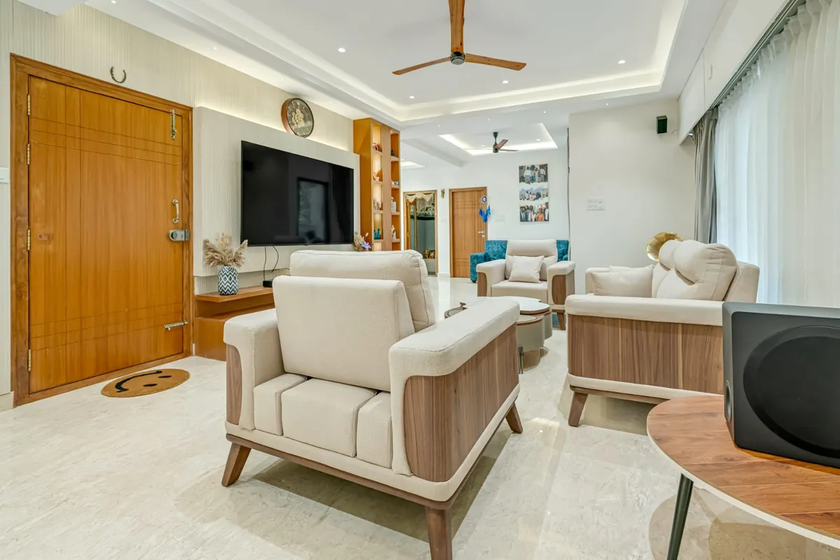 Living room viewed from the teak main door with a horseshoe nailed above it: cream-and-walnut sofa set on cream marble