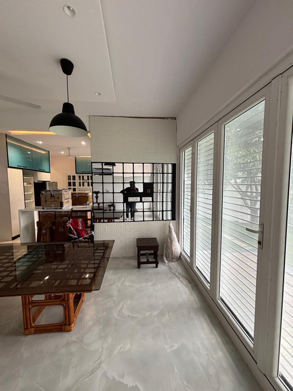 Dining area with a glass-top rattan-base dining table, a black dome pendant light and a white brick-textured accent wall opening to the kitchen.