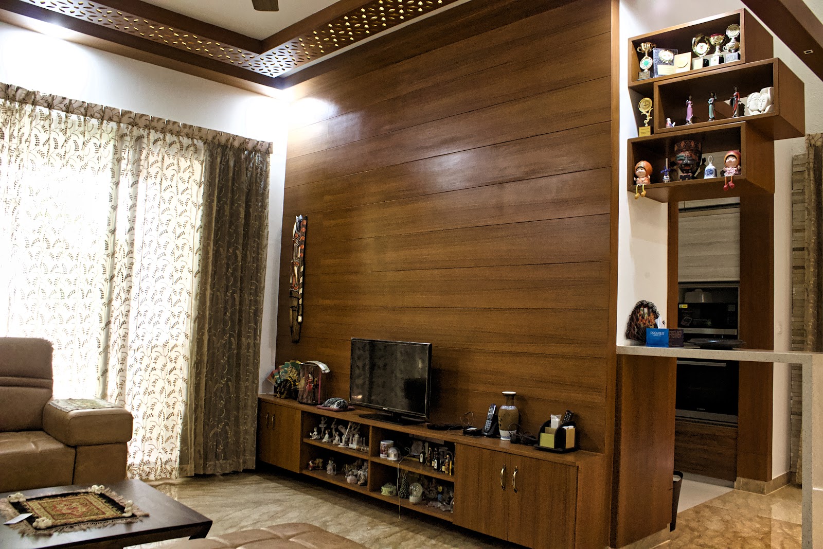 Living room with a full wood-plank panelled TV wall, a wood console displaying curios, jaali-cut cove ceiling trim