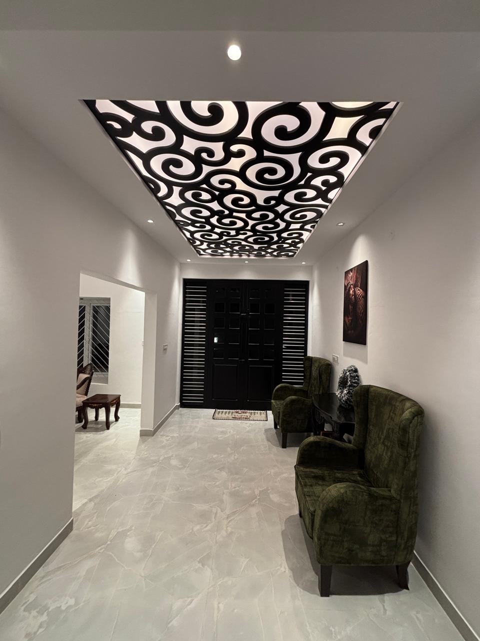 Entrance foyer with a dramatic black CNC-cut backlit false ceiling, a black slatted main door and a pair of dark green velvet wingback chairs.