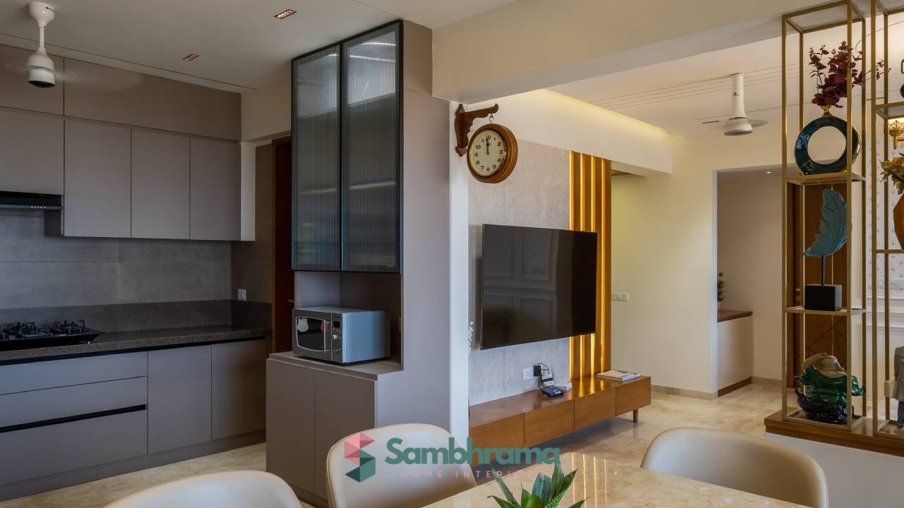 Real photo of an open-plan kitchen and living area with a grey handleless kitchen run, a stone-clad TV wall with vertical brass fluting