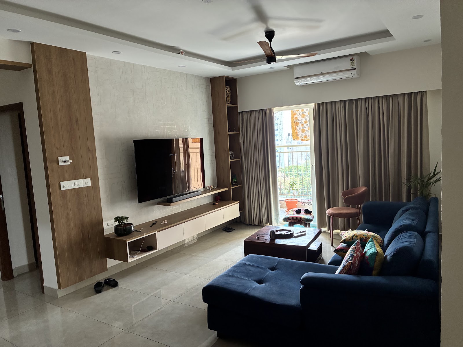 Living room with a navy blue L-shaped sofa and patterned cushions facing a wood-and-textured-wallpaper TV wall with a floating console.
