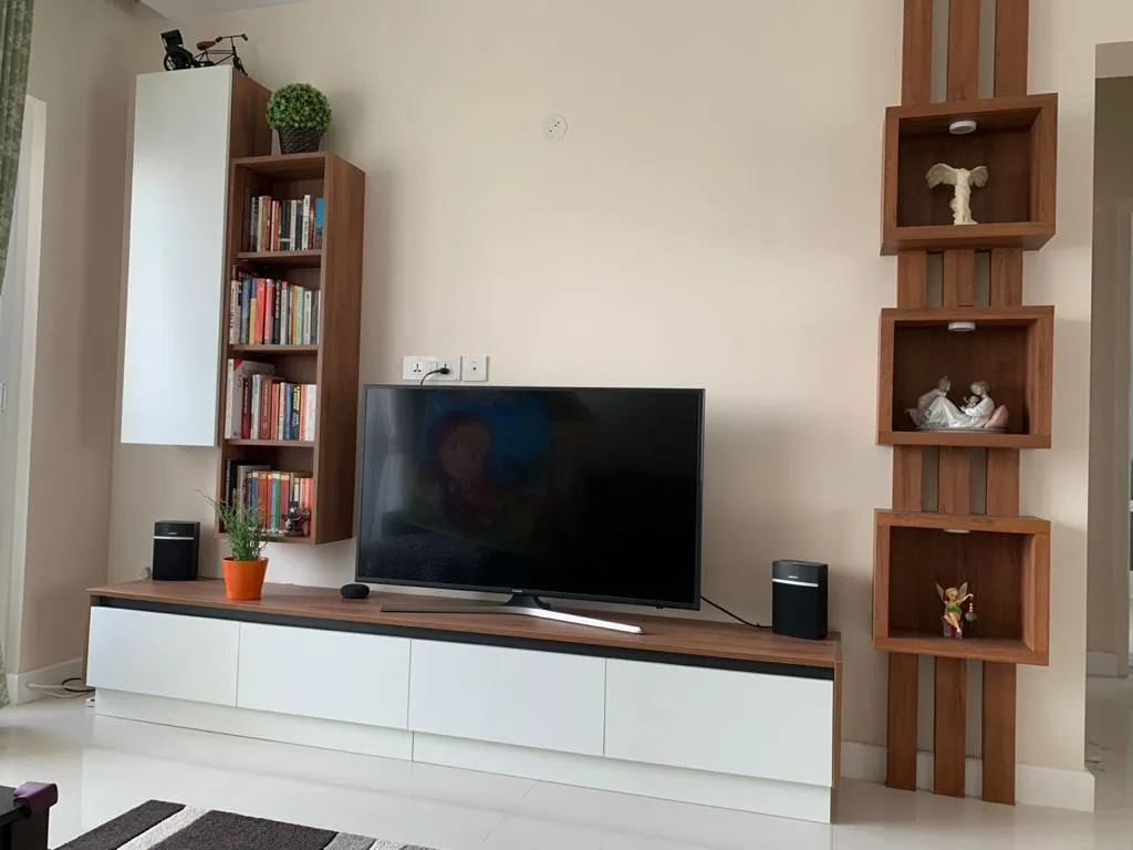 Living-room media wall combining a white and walnut floating drawer console, a slim book tower on the left and three spot-lit walnut display boxes mounted on