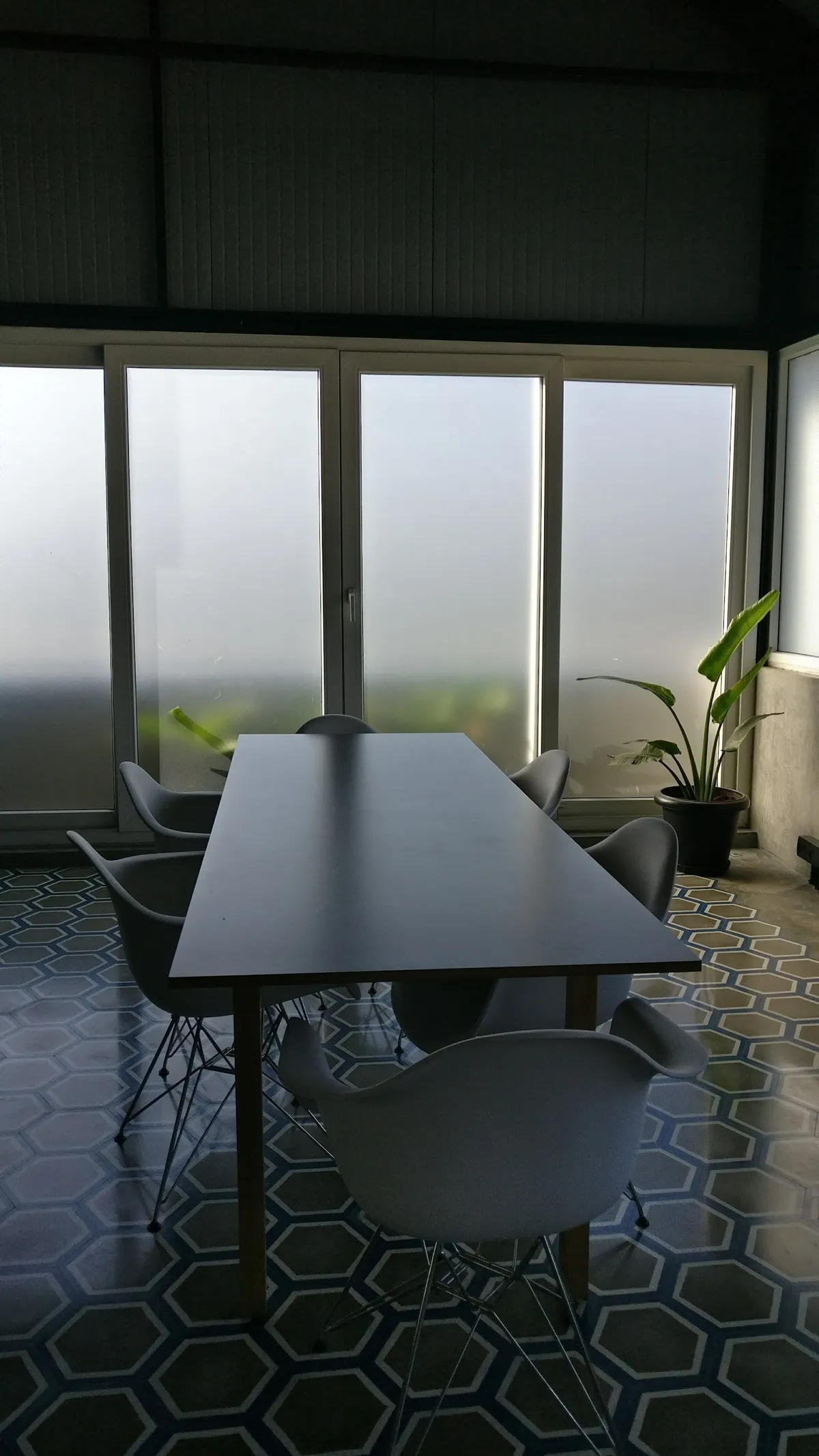 Dining nook with a dark table and mid-century wire-leg chairs on a hexagonal patterned tile floor, backlit by full-height frosted glass doors.