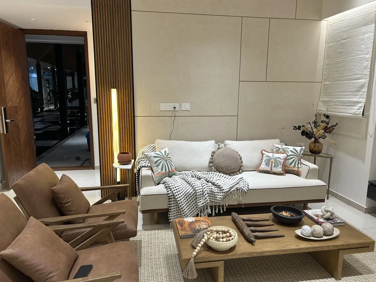 Living room with a stone-panel accent wall, a cream sofa styled with palm-print cushions, leather wood-frame armchairs