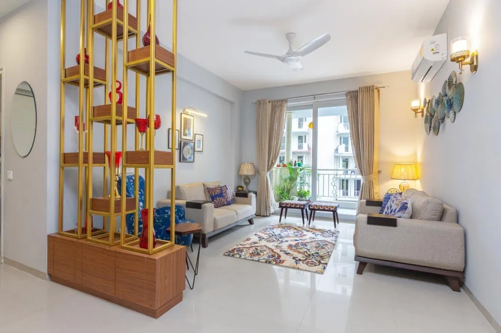 Living room with a tall brass-framed wood shelving console dividing the entry, cream sofas around a printed rug