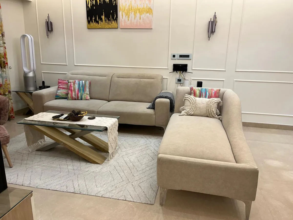Cream fabric sofa with a matching chaise on an ivory diamond flatweave rug, against a white applied-moulding wall hung with two abstract canvases and slim