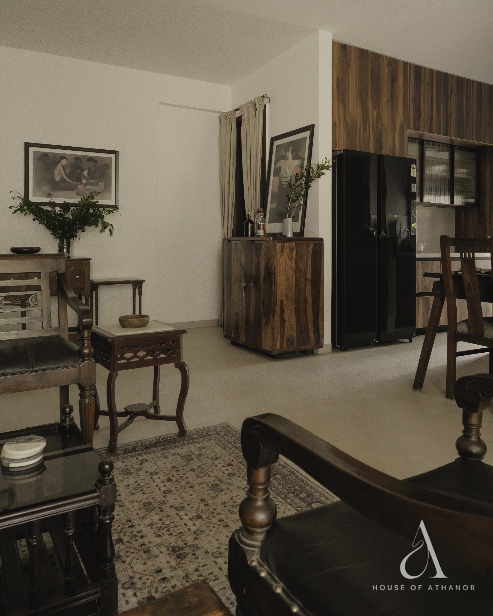 Living room styled with dark wood colonial-era furniture — a carved campaign chair, an inlaid side table and console tables — framed art on cream walls