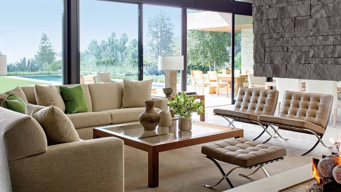 Living room with a beige sectional sofa and tan leather Barcelona chairs and ottoman around a walnut-and-glass coffee table
