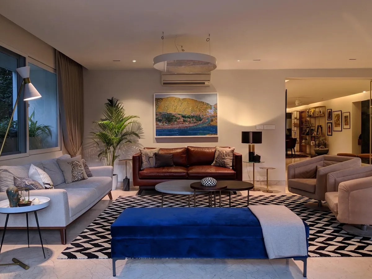 An eclectic living room mixing a brown leather sofa, grey linen sofa and blue velvet bench around nested round coffee tables on a black-and-white chevron rug.