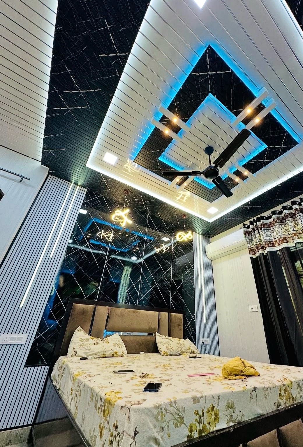 Bedroom with a dramatic multi-tier POP false ceiling in black and white with blue LED trim, a black mirrored feature wall