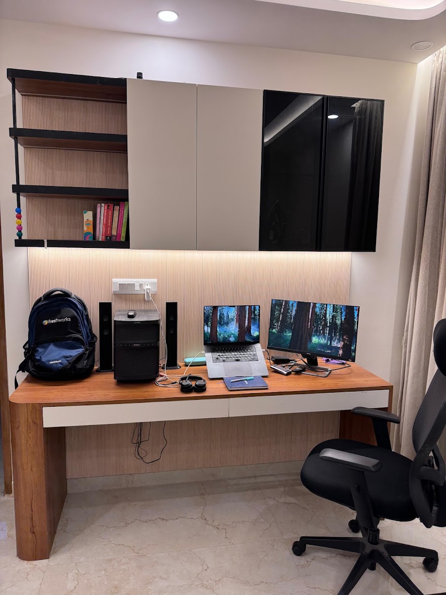 Home study nook with a built-in wood desk against a fluted-panel wall, overhead glossy storage cabinets with under-lit open shelving