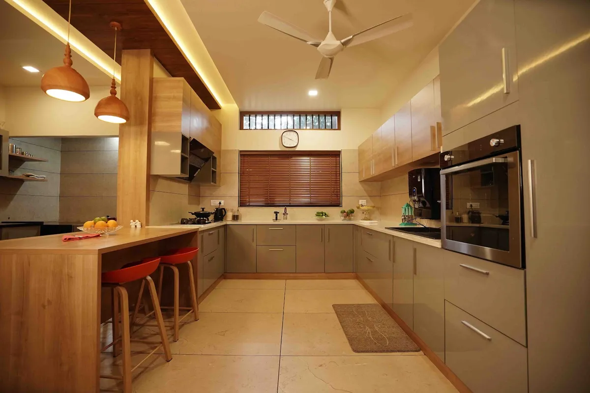 An open kitchen with a wood breakfast counter and red bar stools, twin wood dome pendant lights, a grey glossy L-shaped cabinet run