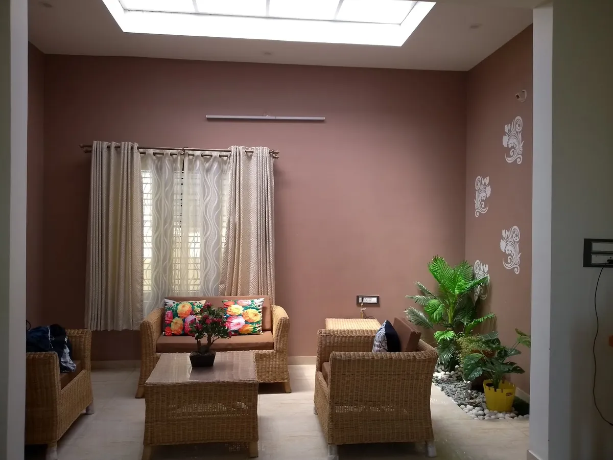 Living room lit by a long ceiling skylight, furnished with a cane sofa set and bright floral cushions against dusty-rose walls stencilled in silver damask
