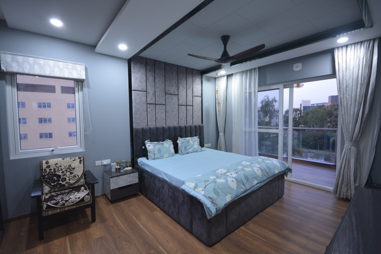 Bedroom with a channel-tufted grey upholstered headboard wall, a floral-cushioned accent chair by the window