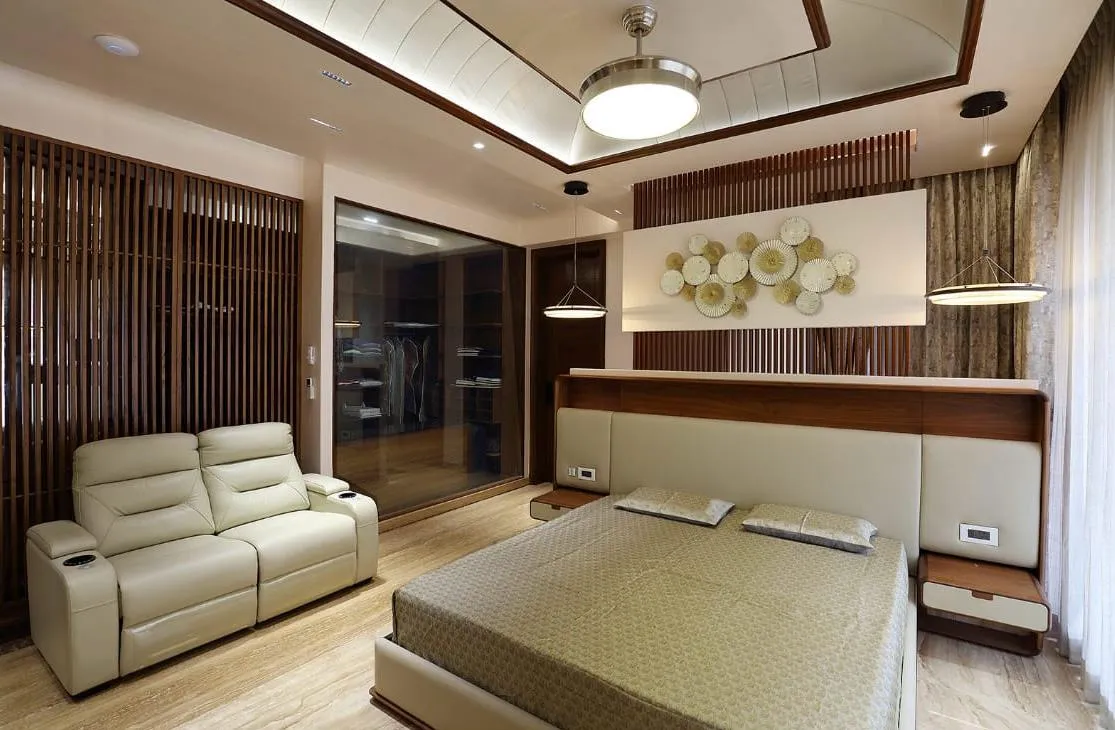 Master bedroom with a fluted wood-slat feature wall behind an upholstered bed, a glass-fronted walk-in wardrobe, and a cream reclining loveseat.