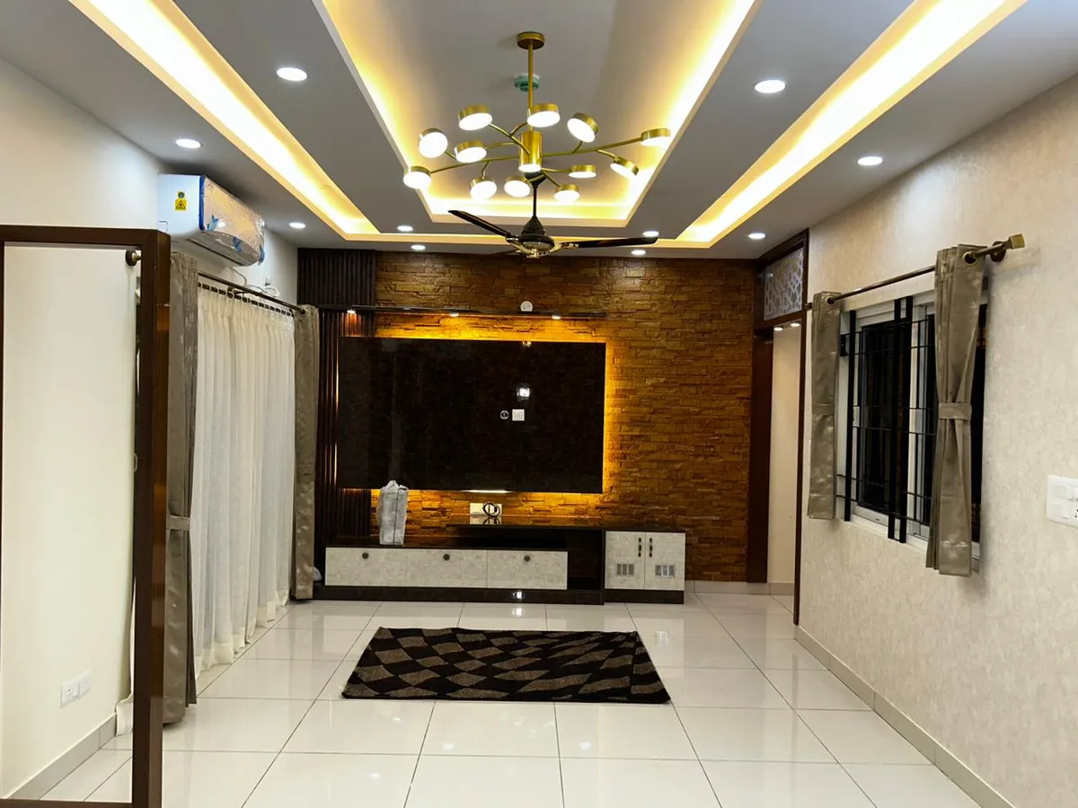 Living room with a stacked-stone-clad TV feature wall lit from behind, a gold sputnik chandelier in a cove-lit ceiling
