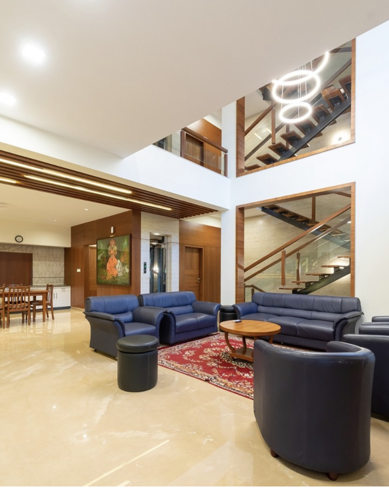 A double-height living lounge with navy leather sofas around a red Persian-style rug