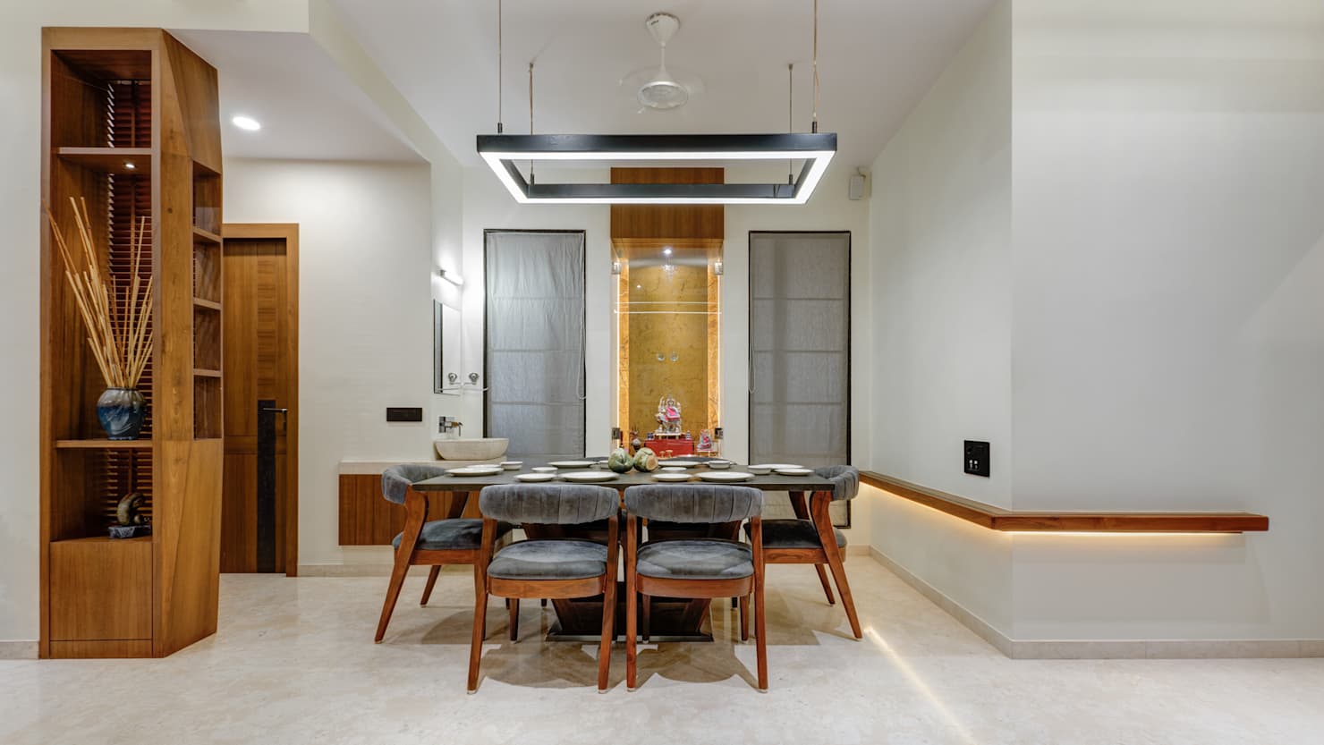Dining area with a rectangular black-framed pendant light over a wood table with grey velvet chairs, a display shelving unit