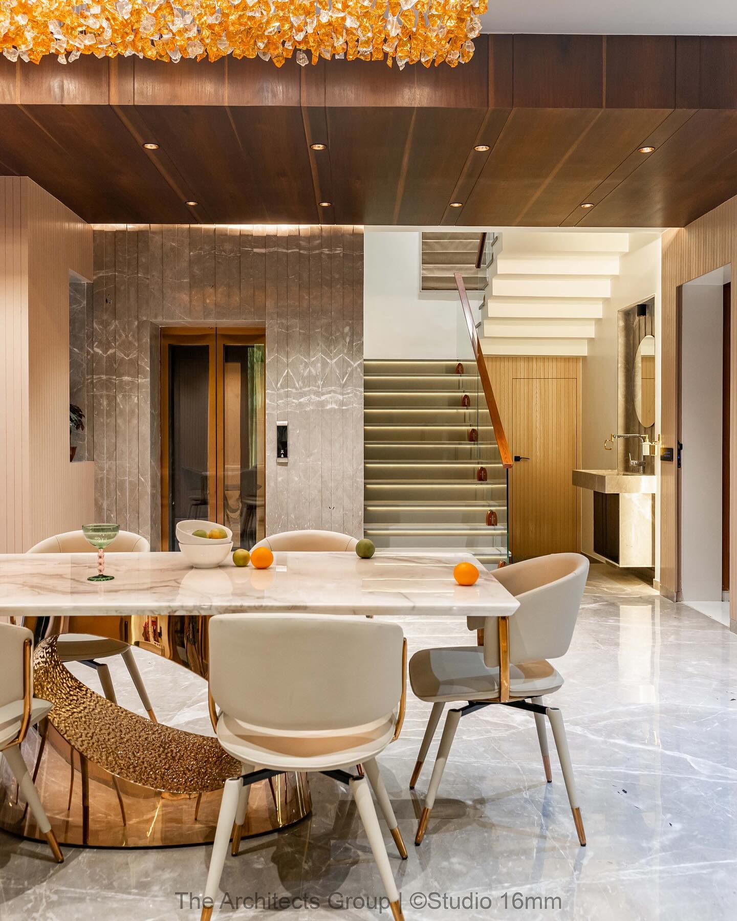 Dining space with a marble-top table on a hammered gold pedestal base, cream leather chairs with gold legs, a wood-panelled ceiling