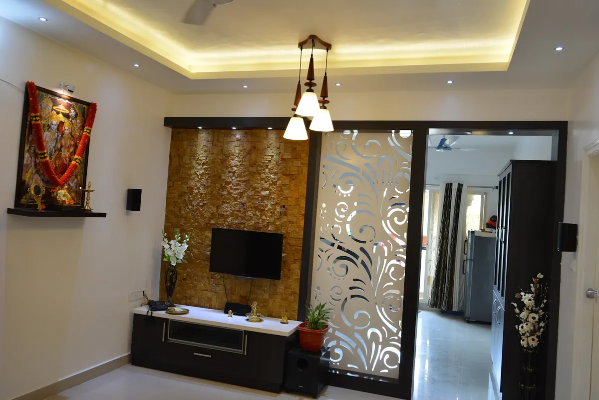 A living room with a stone-clad TV feature wall, a dark wood TV console, and a decorative floral-cutout jaali sliding door leading to the next room