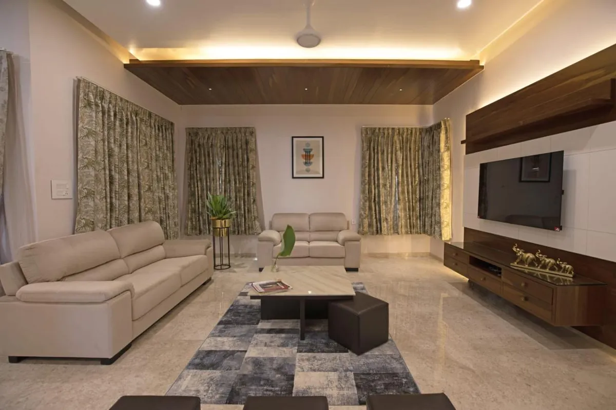 Wide living room with two cream leather sofas facing a white stone TV wall banded in walnut, a slatted wood ceiling raft with cove lighting overhead