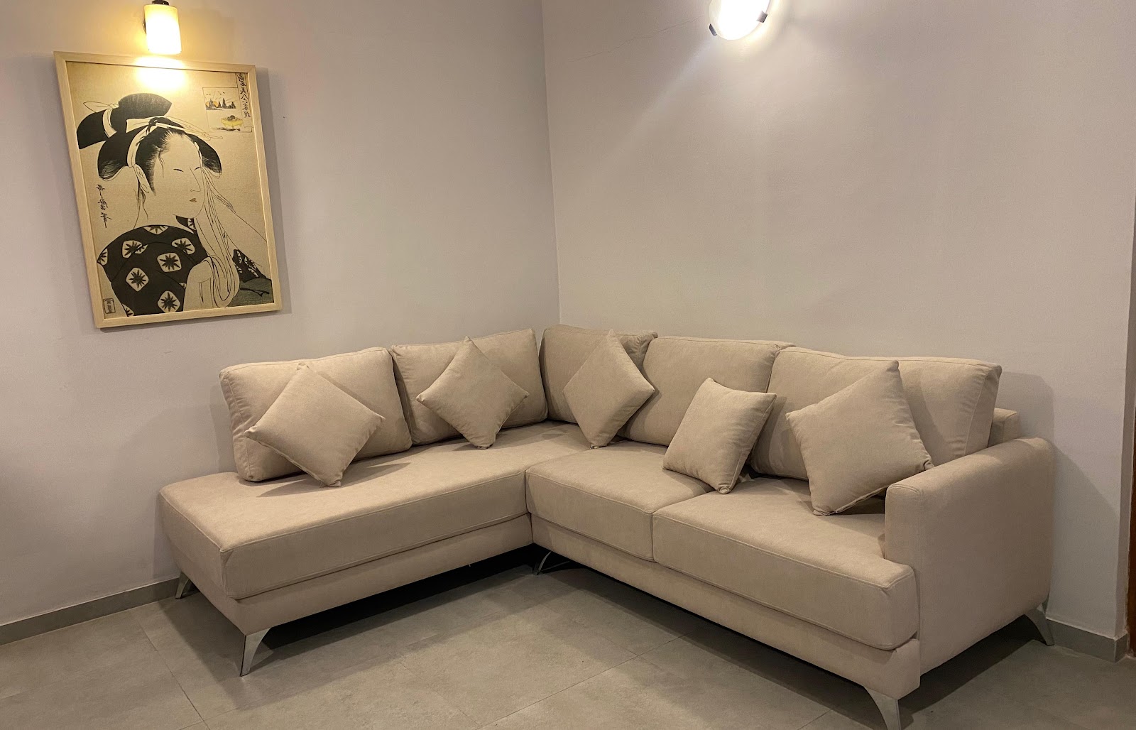 Living room corner with a cream L-shaped sectional sofa piled with matching cushions beneath a framed Japanese woodblock-style print.