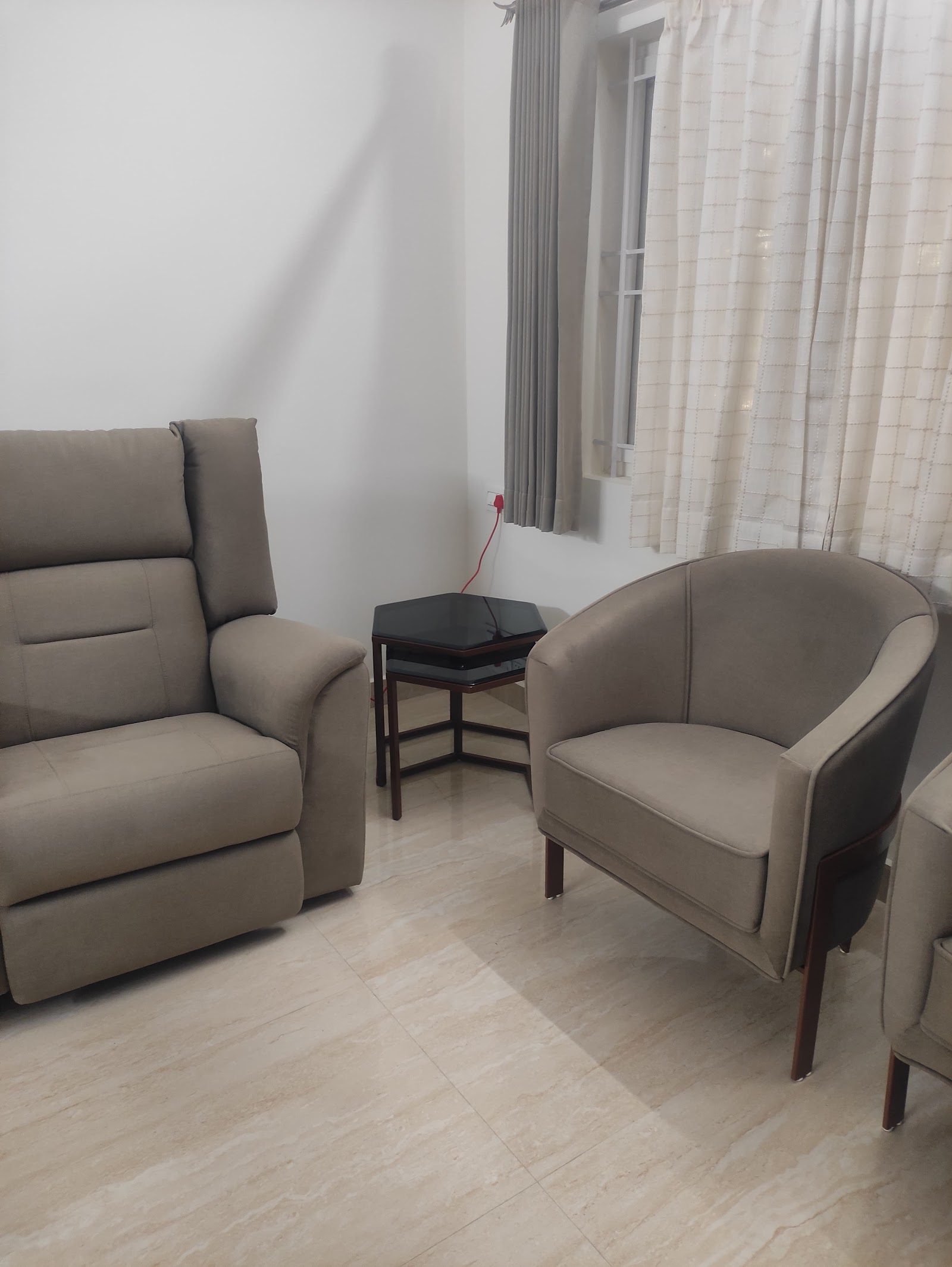 Living room seating corner with a taupe fabric recliner armchair and a matching tub chair around a black hexagonal side table, beneath striped sheer curtains.