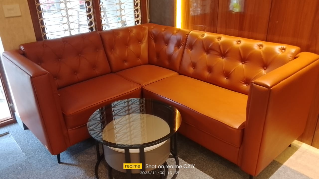 A corner sectional in tufted burnt-orange leather with a round glass coffee table set against dark wood-panelled walls and a metal-grille window.