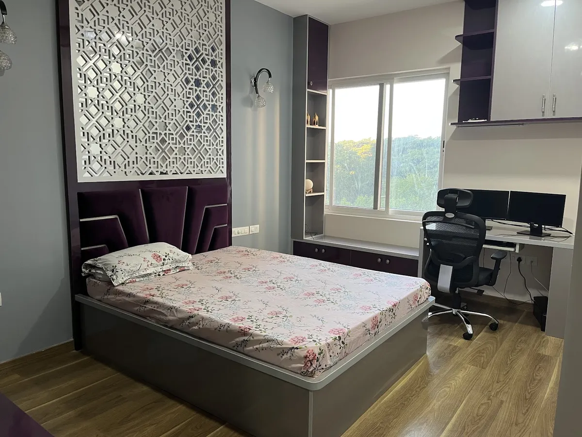 Bedroom with a white CNC-cut jaali panel set into a glossy aubergine headboard wall, purple velvet headboard cushions over a grey storage bed